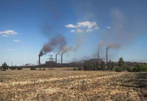 smoking factory pipes against a blue sky and clouds photo