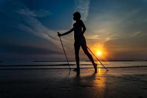 chica flaca al amanecer en la playa hacia el mar con nordic walki foto