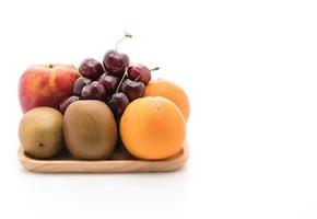 Fruta mixta en placa de madera sobre fondo blanco. foto