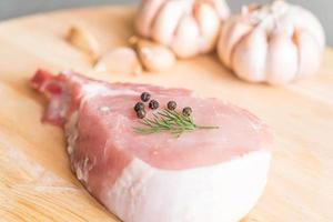 Chuleta de cerdo fresca sobre tablero de madera con ajo y pimientos negros foto