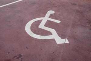 Señal de estacionamiento blanco para discapacitados pintado sobre un piso rojo