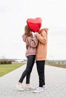 Pareja con globos rojos abrazándose y besándose al aire libre divirtiéndose foto