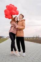 Joven pareja amorosa con globos rojos abrazando al aire libre divirtiéndose foto