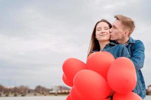 Joven pareja amorosa con globos rojos abrazándose y besándose al aire libre foto