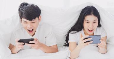 Young couple using phone in bed with cheerful expressions photo