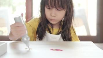 linda chica asiática en delantal está dibujando con pintura brillante multicolor.