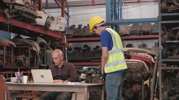 dos hombres en el almacén de repuestos de automóviles. El propietario caucásico usa computadoras portátiles para verificar los pedidos y culpa a un empleado asiático por las fallas de las piezas del motor industrial en una fábrica. video