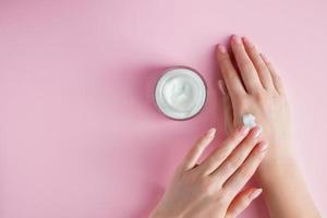 Nourishing cream and beautiful female hands on pink background.