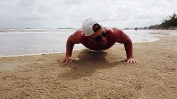 jovem fazendo exercícios pela manhã, flexões na praia video