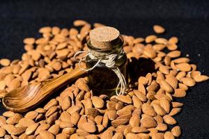 un montón de almendras y un vaso con aceite de almendras foto