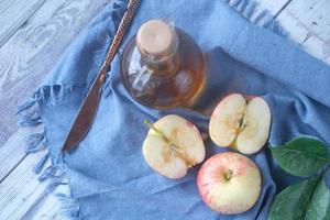 Vinagre de manzana en botella de vidrio con manzana verde fresca en la mesa foto