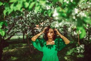 A young girl is standing in the park under a blossoming apple tree photo