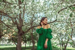 A young girl is standing in the park under a blossoming apple tree photo