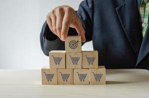 Hand holding wood cube with icon goal and shopping cart photo