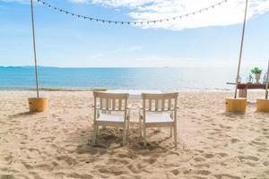 Mesa y sillas blancas en la playa con vistas al mar azul y al cielo despejado foto