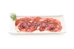 Carne de cerdo fresca en rodajas con salsa sobre fondo blanco.