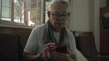 mensaje de texto de anciano sano en el teléfono inteligente en la sala de estar.