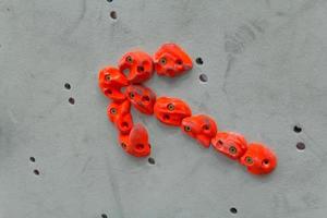 Red climbing holds in the shape of an arrow on grey wall photo