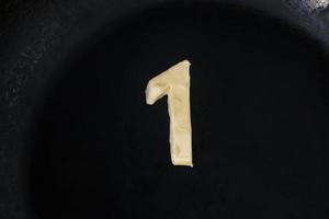 Mantequilla en forma de número 1 en sartén caliente - Vista superior de cerca