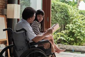 Granddaughter sat on the old Asian grandfather's lap in wheelchair. photo