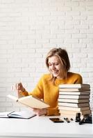 Joven mujer sonriente en suéter amarillo leyendo un libro y riendo foto