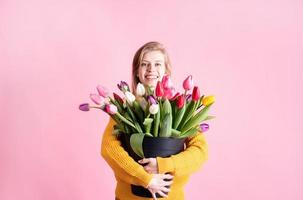 woman holding a bucket of fresh tulips isolated on pink background photo