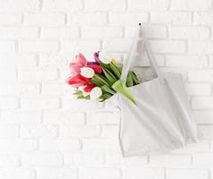 Gray fabric bag full of colorful tulips on white brick background photo