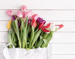 Gray fabric bag full of colorful tulips on white wooden background photo