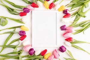 White frame with colorful spring tulips top view over white background photo