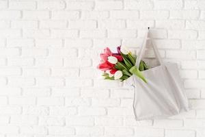 Gray fabric bag full of colorful tulips on white brick background photo