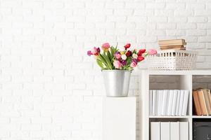 Bucket of tulip flowers next to the bookshelf photo