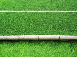 Texture of plastic artificial grass and concrete border of school yard photo