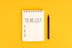 To do list in spiral notepad isolated on yellow background. Top view photo