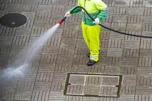Worker holding a hose cleaning a sidewalk with water photo
