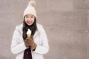 Joven mujer asiática sonríe y feliz con helado en la temporada de invierno con nieve foto