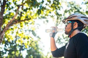 Cyclists stand on the top of the mountain and drink a bottle of water.