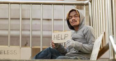 Hombre sin hogar sentado y sosteniendo el cartel de ayuda en el paso elevado