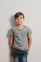 un niño con cara de miedo junto a la pared blanca, camisa gris, jeans foto