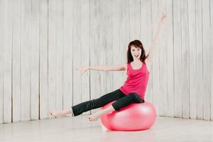 una chica con un top rosa, sentada en una fitball rosa en un gimnasio foto