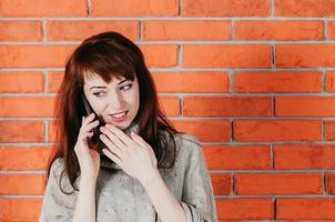 Pretty woman talking by cellphone, smiling, brick wall in the backdrop photo