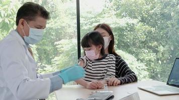 Médico varón vacunando a una niña asiática en la clínica de pediatría. video