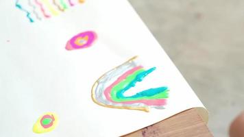 A close-up shot of a child's hand drawing by glitter paint in multi colors and beautiful on white paper It is an art learning, hobbies at home to practice design skill to be creative with happiness. video