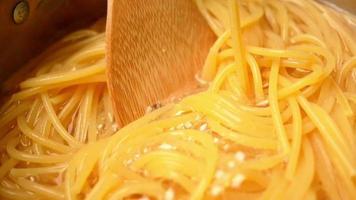 Raw spaghetti is being cooked in boiling water in a kitchen pot. video