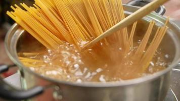 Raw spaghetti is being cooked in boiling water in a kitchen pot. video