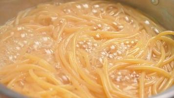 Raw spaghetti is being cooked in boiling water in a kitchen pot.