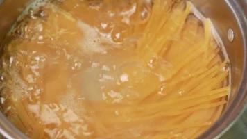 espaguetis crudos se cocinan en agua hirviendo en una olla de cocina. video