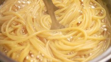 Raw spaghetti is being cooked in boiling water in a kitchen pot. video