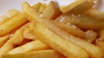 Nahaufnahme der Hand mit Salz auf Pommes frites bestreut. video