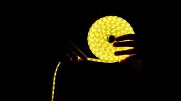 Yellow LED strip coil decorative lighting in hand on dark background video