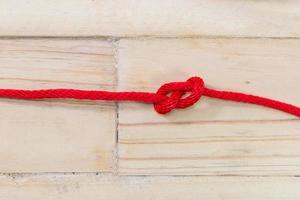 Nudo en forma de ocho hecho con cuerda roja sobre fondo de madera